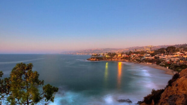 A scenic view of Malibu California coastline at dusk with calm ocean and illuminated houses