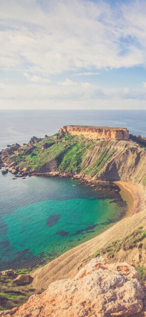 A stunning view of Malta coastline with turquoise water and rocky cliffs covered in greenery