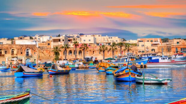 Traditional Malta boats docked at the harbor with historic buildings in the background