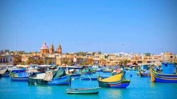 Traditional Maltese boats floating on clear blue water near waterfront buildings in Malta harbor
