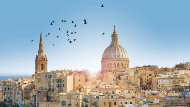 Historic architecture in Malta with a flock of birds flying above the cityscape