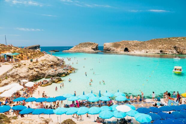 Turquoise crystal clear water at a Malta beach with sun umbrellas and people relaxing on the shore