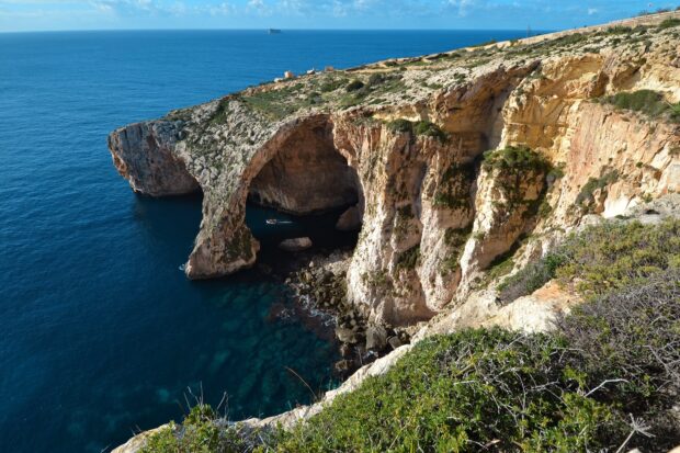 Natural rock arch formation in Malta with clear blue sea and green shrubs