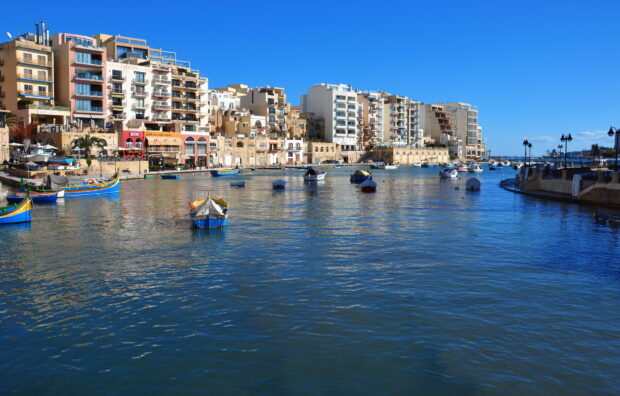 Traditional Malta harbor with colorful boats and modern buildings along the waterfront