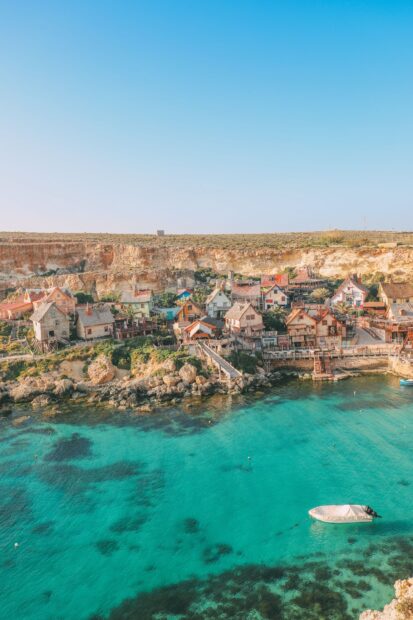 A charming Malta village by the clear turquoise sea with rocky coastline and small boat