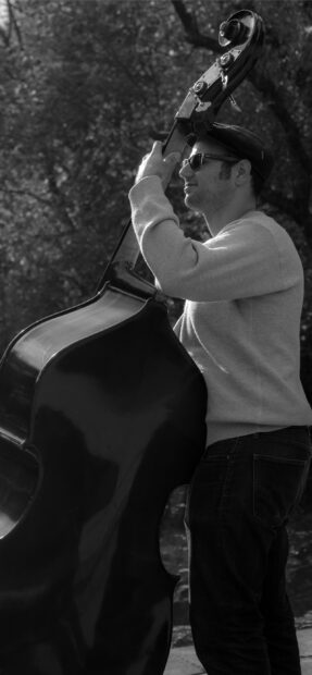 A man is playing a double bass while standing outside in a natural setting, 2K Mobile Wallpaper