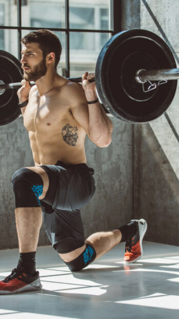 A man is doing weighted lunges using a barbell to strengthen muscles in a gym, HD Mobile Wallpaper