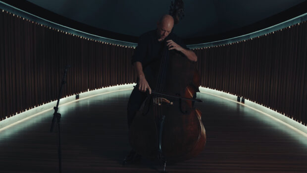 A man is focused on playing a double bass in a dimly lit curved room with wooden floors, HD Desktop Wallpaper