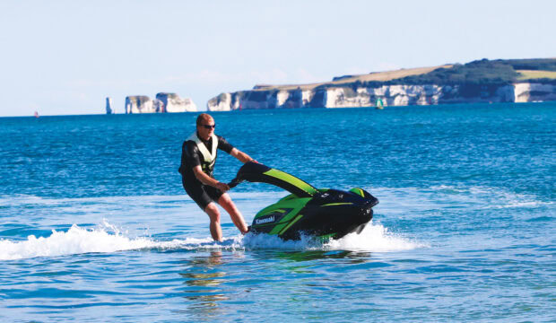 A man enjoys riding a green jet ski near cliffs on a sunny day, HD Desktop Wallpaper