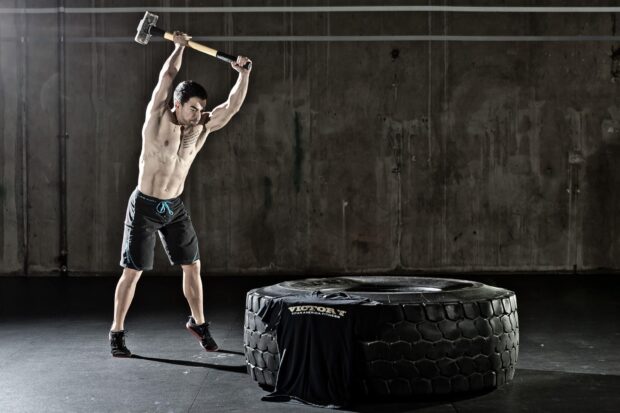 A man is intensely swinging a sledgehammer near a large tire in a Crossfit training session, HD Desktop Wallpaper