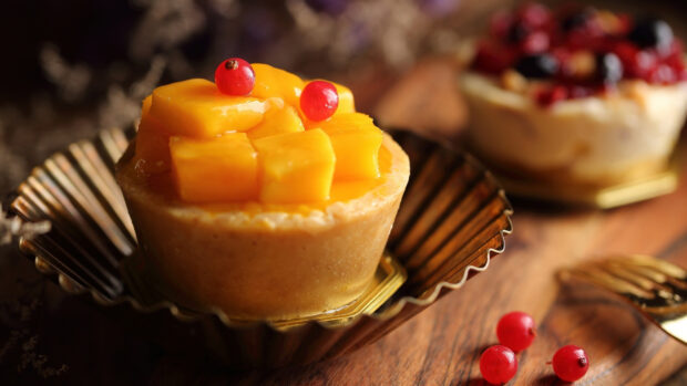 A close up of mango dessert topped with red berries on a wooden table with a warm background, 4K Desktop Wallpaper