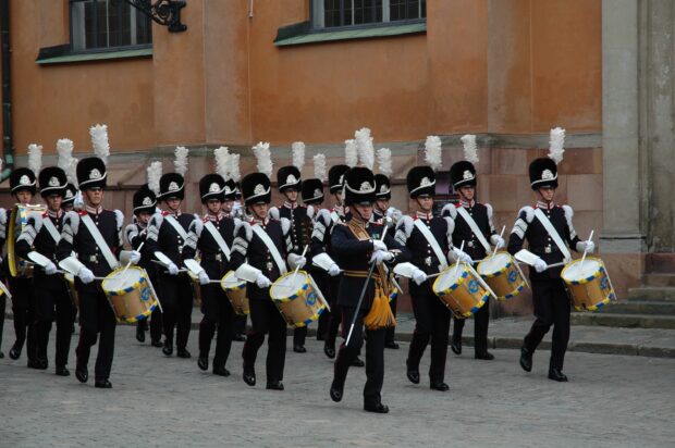 A marching band wearing traditional uniforms plays drums in a street parade, 2K Desktop Wallpaper