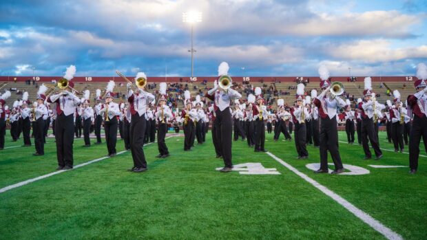A marching band is playing instruments on a green football field under cloudy skies, HD Desktop Wallpaper