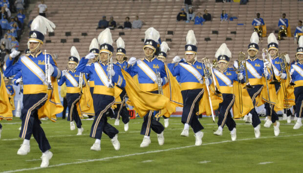 A marching band in blue and yellow uniforms is performing on a football field with musical instruments, 2K Desktop Wallpaper
