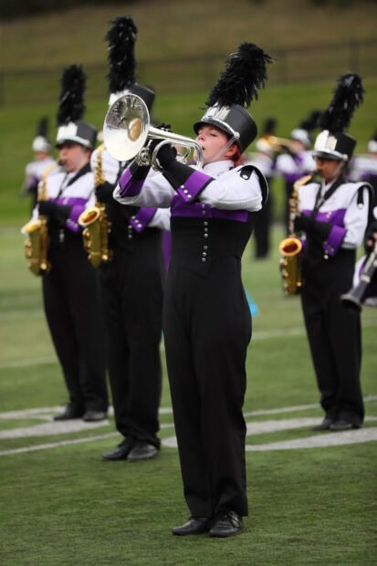 A marching band trumpet player performs on field with others in colorful uniforms, 2K Mobile Wallpaper