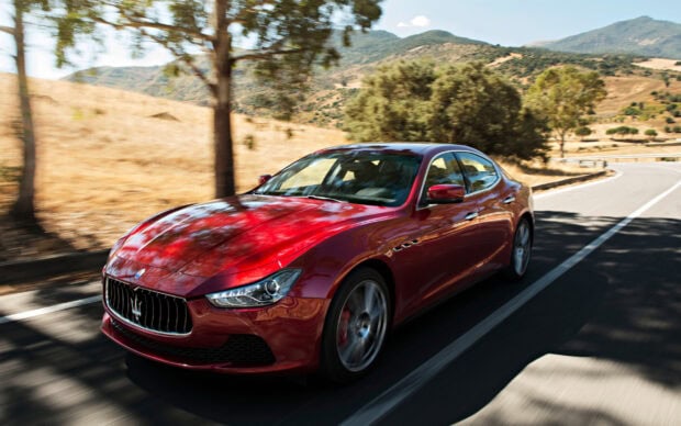 Red Maserati car driving fast on a curved mountain road