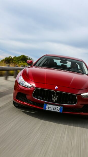 Red Maserati driving fast on a road with blurred background and clear sky