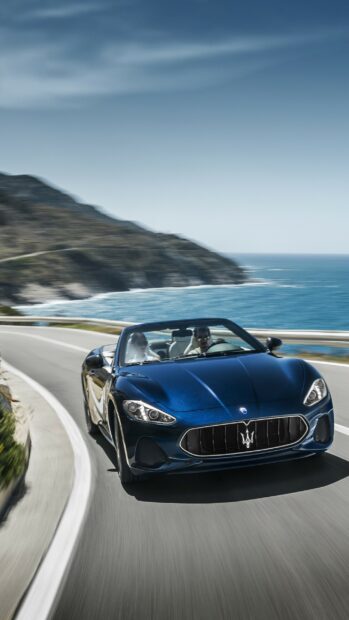 Luxury Maserati car driving along coastal road with ocean and mountains in background