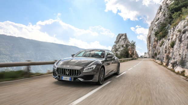 A sleek Maserati driving on a mountain road with rocky cliffs and blue sky background