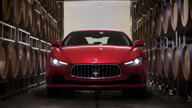 A red Maserati car parked inside a cellar with wooden barrels on both sides