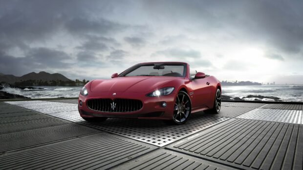 Red Maserati convertible car parked near the ocean with mountains in the background