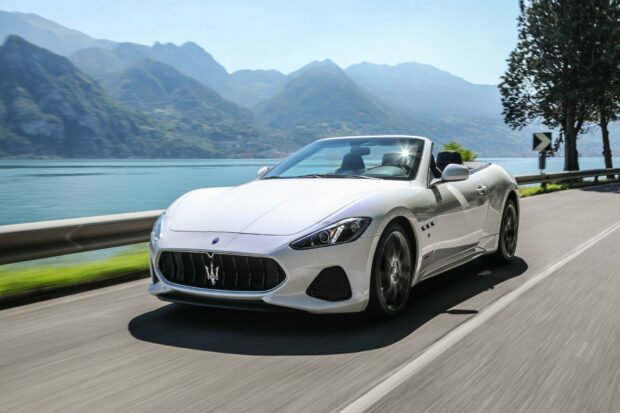 White Maserati convertible driving on a lake side road with mountain background