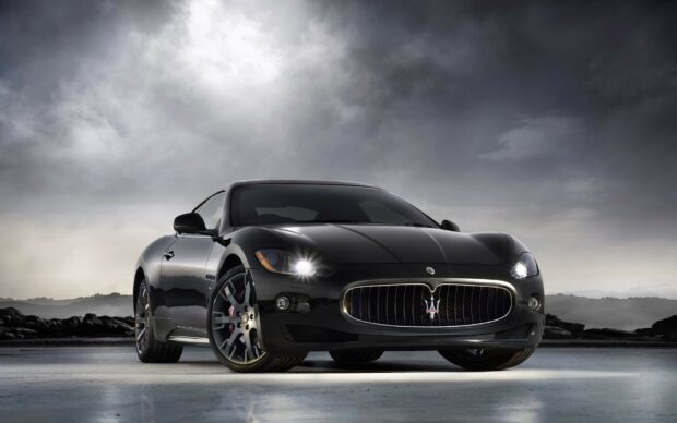 Black Maserati car standing on a concrete surface under a cloudy sky