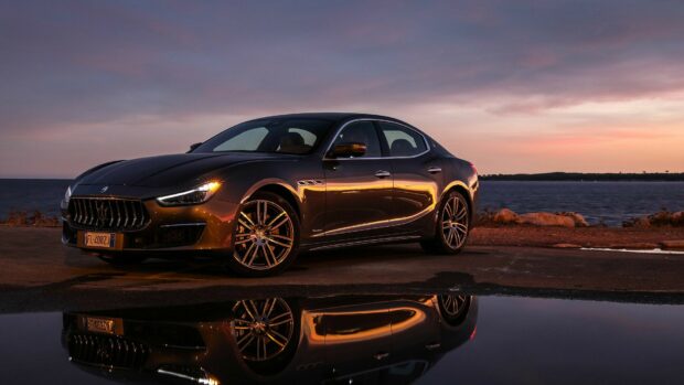 Maserati luxury sedan parked by the sea during sunset with clear reflection on wet surface