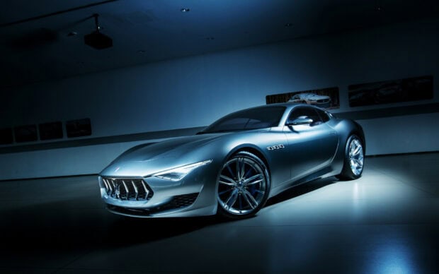 A silver Maserati car showcased in a dark room with blue lighting highlighting its sleek design