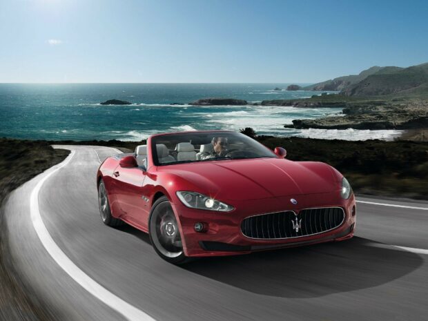 Red Maserati car driving on coastal road under clear sky