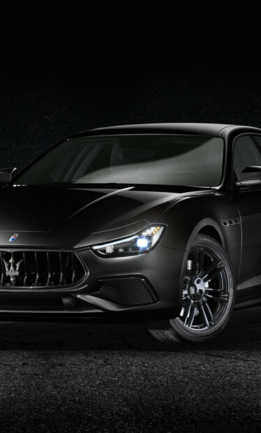 Black Maserati car front view with illuminated headlight on dark background