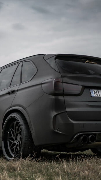 A matte black BMW X5 with dark tinted windows is parked on grass under an overcast sky, 4K Phone Wallpaper