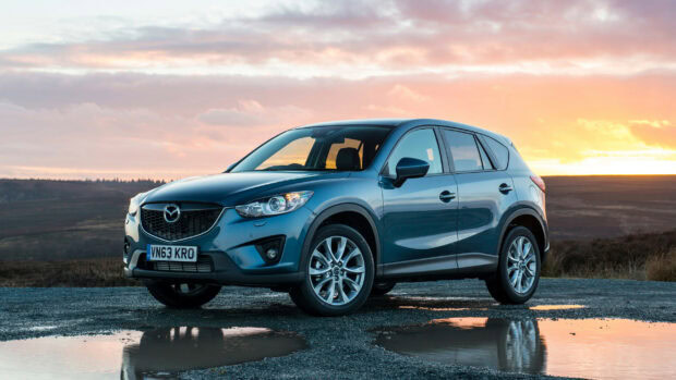 A blue Mazda is parked on a wet road with a sunset sky in the background, 2K Desktop Wallpaper