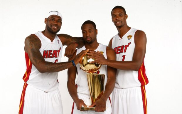Three Miami Heat players holding the NBA championship trophy in team uniforms