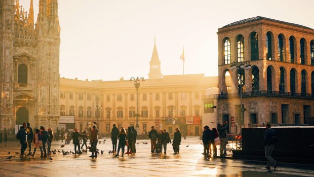 People gathering in Milan city square near historic buildings in warm sunlight