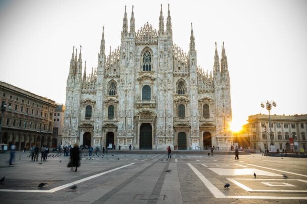 The Milan cathedral stands majestically in the sunset with people walking around the square