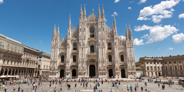 The Milan cathedral with many people walking in the plaza under a clear blue sky