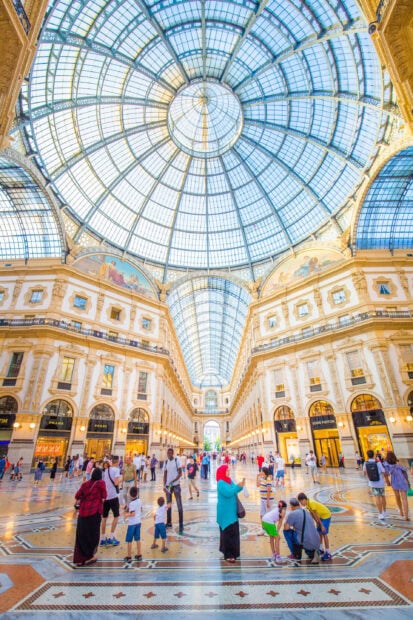 The interior view of Milan with a large glass dome and people walking inside the gallery