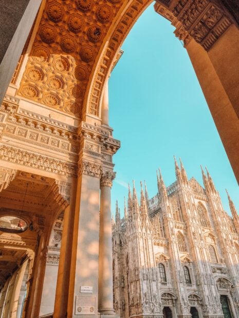 Ornate architectural details of Milan cathedral and arch under blue sky