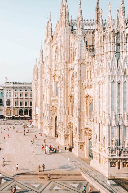 A detailed view of Milan cathedral with tourists walking around the square in bright sunlight