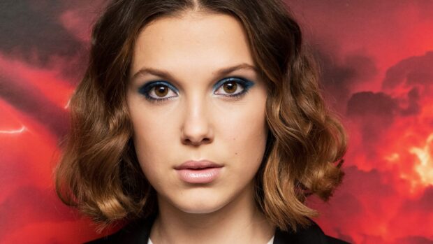 Millie Bobby Brown looks directly into the camera with a red smoky background, 4K Desktop Wallpaper