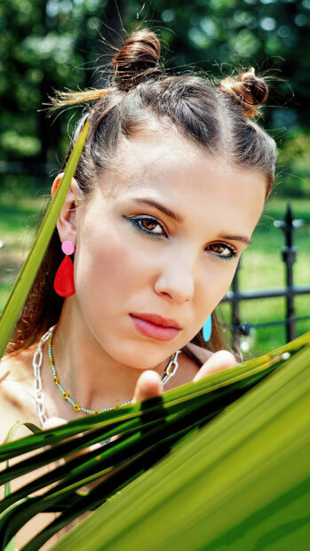 A close up portrait of Millie Bobby Brown with colorful earrings and braided hair outdoors, 4K Mobile Wallpaper