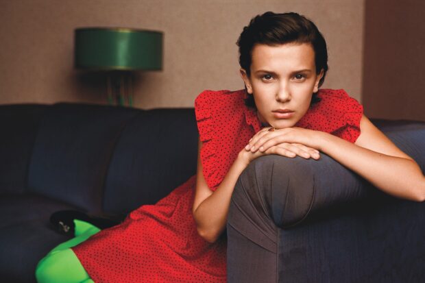 Millie Bobby Brown leans on a couch armrest with a focused expression, 2K Desktop Wallpaper