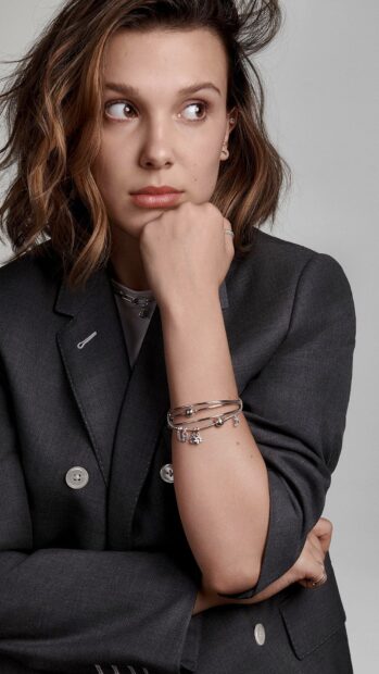 Millie Bobby Brown looks thoughtfully to the side wearing a dark suit and silver jewelry, HD Mobile Wallpaper