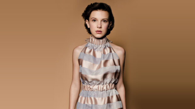Millie Bobby Brown stands wearing a striped halter dress against a brown background, HD Desktop Wallpaper