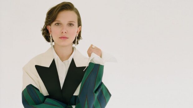 Millie Bobby Brown stands confidently wearing a unique striped blazer and earrings, HD Desktop Wallpaper