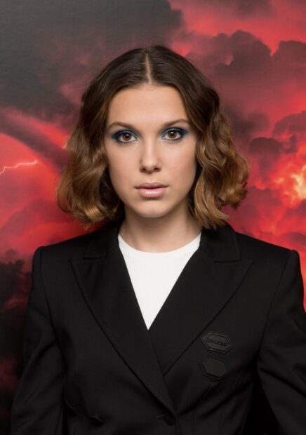 Millie Bobby Brown stands before a red stormy sky with focused eyes, HD Desktop Wallpaper