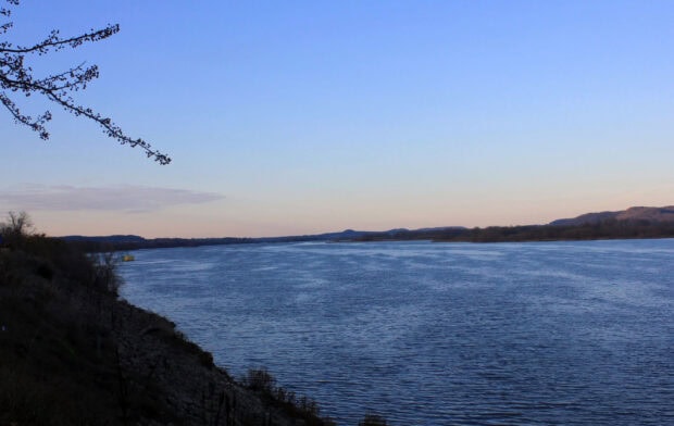 The Mississippi River stretches wide under the clear evening sky with distant hills, 2K Desktop Wallpaper