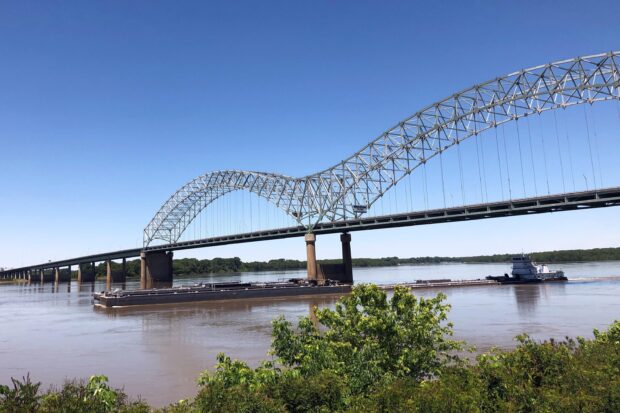 A steel arch bridge spans the Mississippi River over a cargo boat on a clear day, 2K Desktop Wallpaper