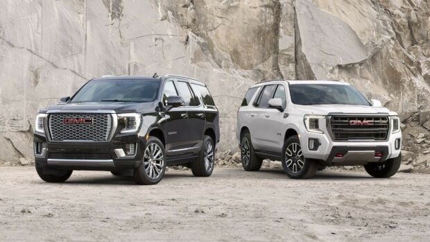 Two GMC SUVs are parked in front of a rocky cliff, showcasing their bold designs and off road capability, HD Desktop Wallpaper